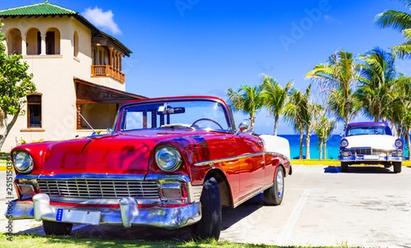 Fototapeta Roter amerikanischer Cabriolet  Oldtimer und ein blau weisser Oldtimer parken am Strand von Varadero in Cuba - Serie Kuba Reportage