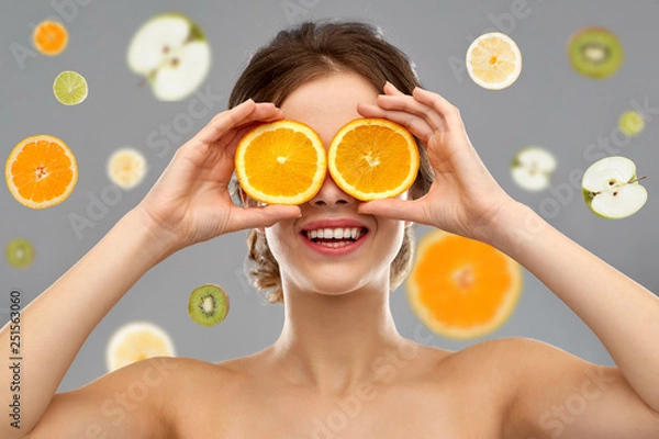 Fototapeta beauty and people concept - smiling young woman with oranges on eyes over grey background and citrus fruits