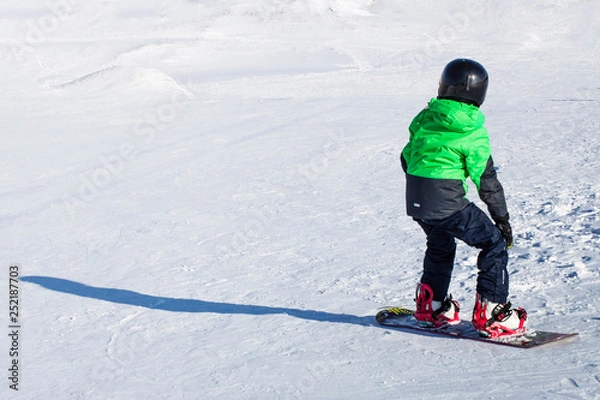 Fototapeta Kid on snowboard in winter sunset nature. Sport photo with edit space