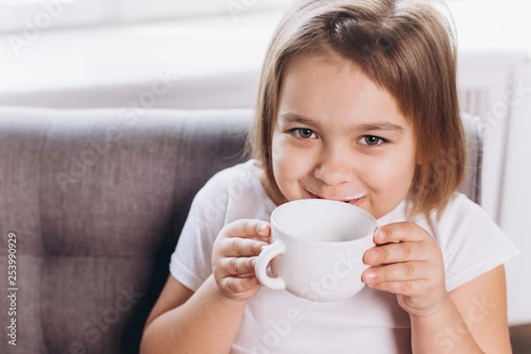 Fototapeta Cheerful cute adorable girl drinking milk in a cup at home