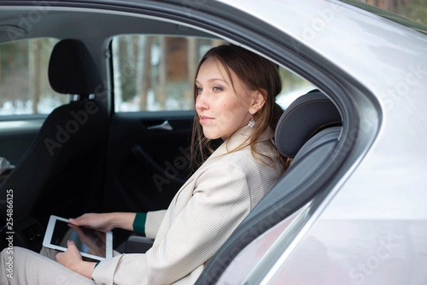 Fototapeta Attractive executive female manager working with a tablet in a backseat of a car