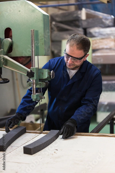 Fototapeta Portrait of a young man in a furniture factory cutting the foam for the sofa