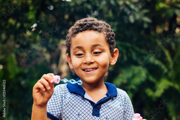 Fototapeta Smiling Brazilian child playing with soap bubbles in the home garden. Boy happy. Lifestyle. Children's Day