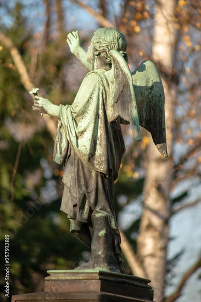 Fototapeta Grüne Bronzeplastik eines Engel auf Podest von hinten (Seitenansicht) auf dem Dorotheenstädtischen Friedhof in Berlin