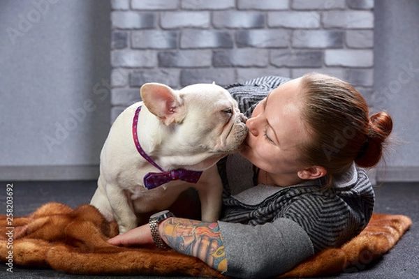 Obraz Young beautiful woman hugging her french bulldog puppy and kissing him - love, friendship concept