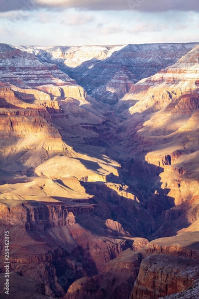 Fototapeta A winter evening in the Grand Canyon with snow in the high elevation and dramatic sunlight and shadows being cast into the canyon.