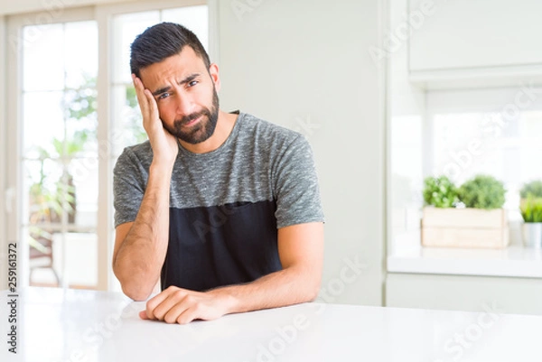 Fototapeta Handsome hispanic man wearing casual t-shirt at home thinking looking tired and bored with depression problems with crossed arms.