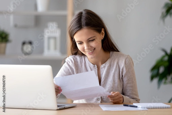 Fototapeta Happy satisfied woman sitting at desk reading positive letter