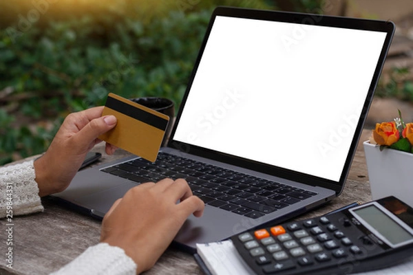 Fototapeta Mock up woman hand holding gold credit card and working on laptop computer for online shopping and payment with calculator on table. Internet banking, e commerce concept.