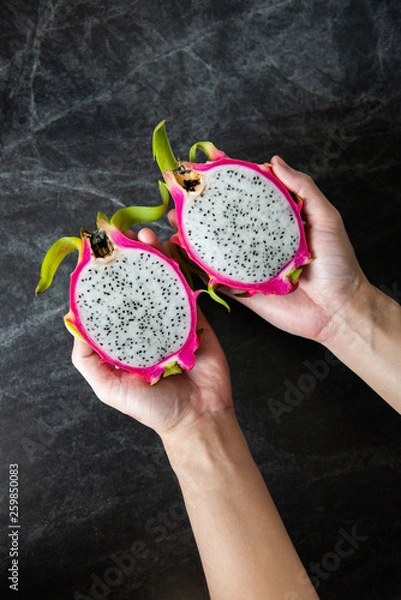 Fototapeta Dragon fruit in man hands with black marble background, top view.