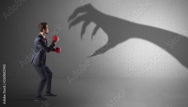 Fototapeta Tiny businessman fighting with scary hand shadow
