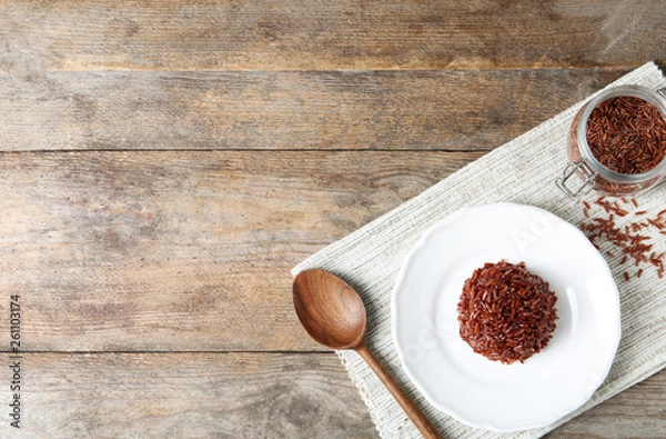 Fototapeta Flat lay composition with plate of boiled brown rice and space for text on wooden background