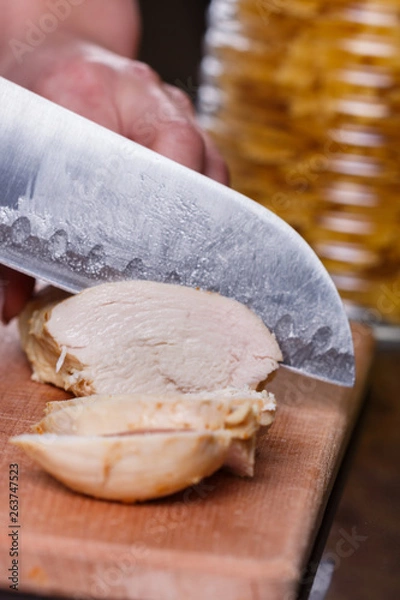 Fototapeta young woman in a gray apron cuts chicken breast