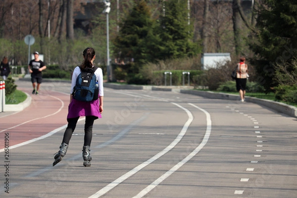 Fototapeta Roller skating, girl with a backpack riding on rollers on a street. Concept of sport, healthy lifestyle