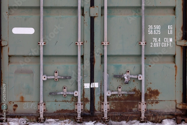 Fototapeta The doors of a large old container are painted in close-up in green with rust, with pipe-type locks and white lettering indicating its characteristics. Transportation and customs cargo.