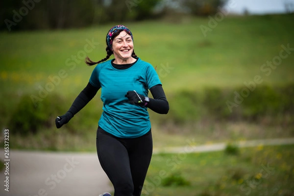 Fototapeta Senior woman in 50s exercising and keeping fit by running in a park