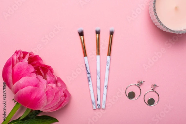 Fototapeta Women's makeup brushes and earrings with a beautiful flower peony on a pink background