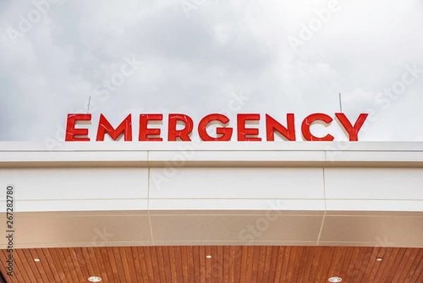 Fototapeta A prominent red 3D all-caps lighted emergency directional sign and marker perched on the awning and canopy of the main hospital entrance.