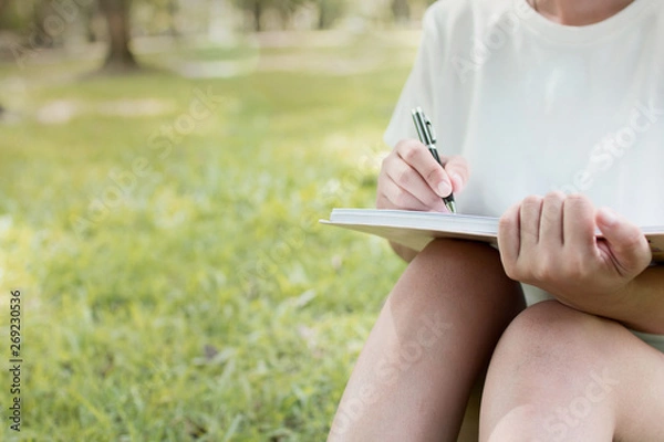 Fototapeta woman 's hand writing  on notebook on green nature background