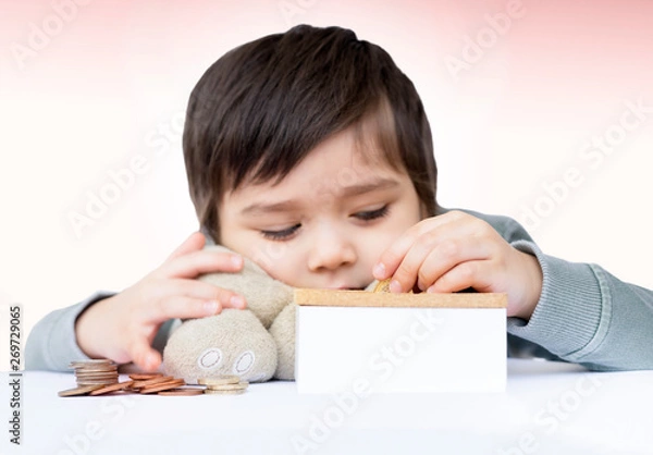 Fototapeta Selective focus of a little boy putting pound coin on a moneybox, Blurry face of cute boy counting his saved coins and thinking about somethings,Child learning about saving concept