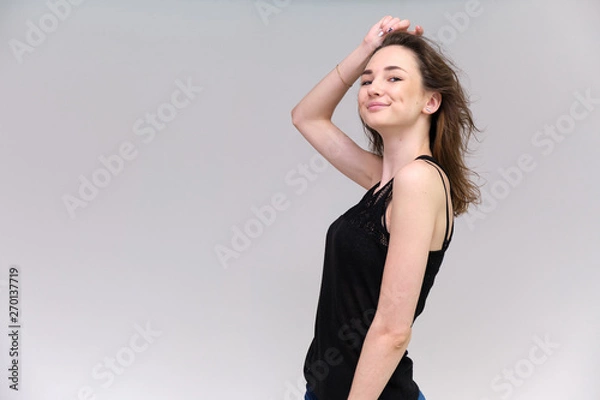 Fototapeta Life is a success. I am pleased with myself. Concept photo of a happy smiling woman satisfied life contented brunette girl in a black T-shirt and jeans on a gray background with flowing hair.