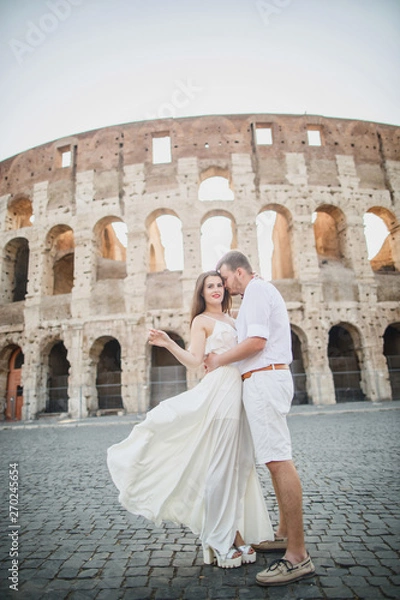 Fototapeta young beautiful couple in white clothes stands against the background of the Colosseum in Rome in Italy