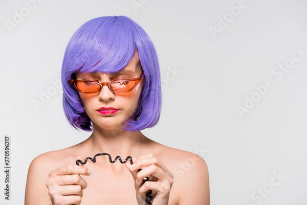 Fototapeta attractive girl in purple wig looking at cord of vintage telephone, isolated on grey