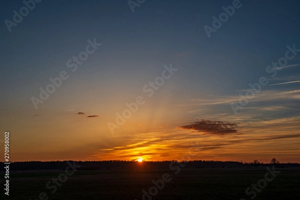 Obraz dramatic red sunset colors in the sky above trees and fields