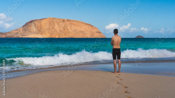 Fototapeta Man standing on an empty pristine beach, enjoying the summer sun and the warm turquoise water. La Conchas beach (Playa de las Conchas) on La Graciosa Island, Canary, Spain.