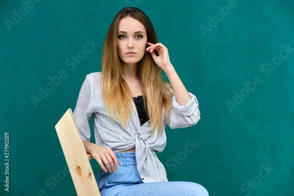 Fototapeta Picture a portrait of a beautiful girl woman with long dark flowing hair, fashionable, on a green background sitting on a wooden staircase. She sits in different poses and smiles.