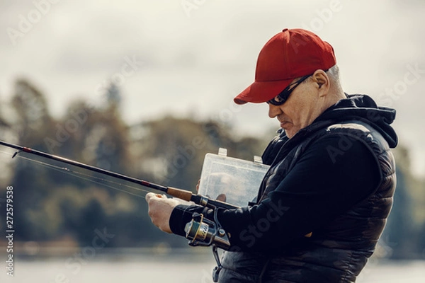 Fototapeta Elderly man enjoys fishing by the river in the summer.