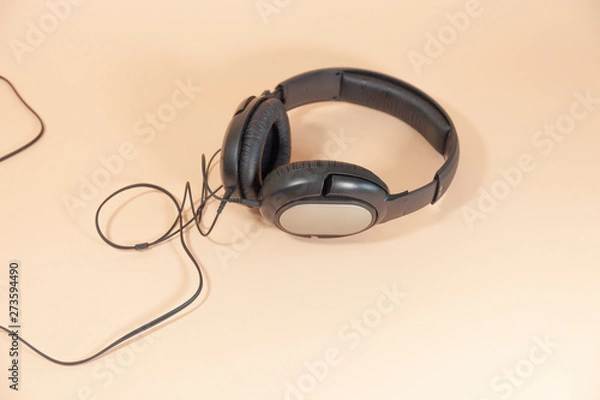 Fototapeta A pair of black headphones with a cord are laying on a pink surface