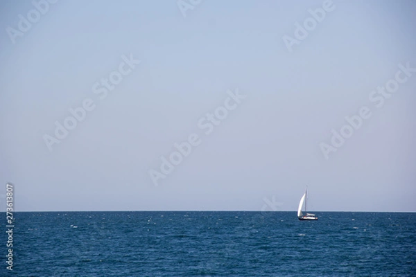 Fototapeta Small sailing yacht with big white sails in the open sea on the horizon