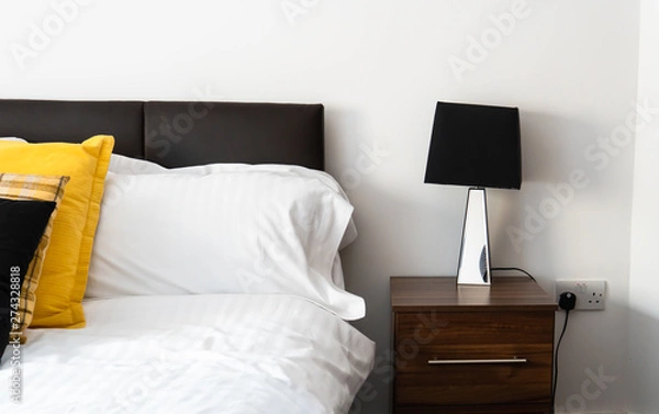 Fototapeta Pillows, cushions on the bed with side table and a lemp decorated the bedroom interior.