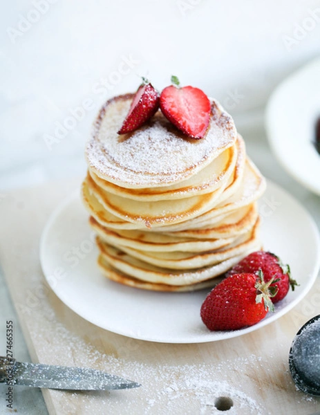 Fototapeta breakfast a stack of lush pancakes with strawberries on a white plate on a light background