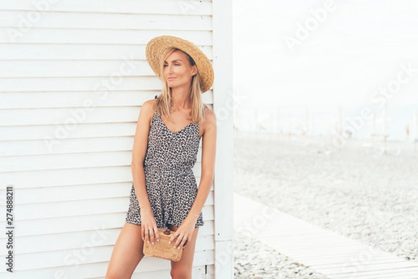 Fototapeta Chic gorgeous tanned blonde girl in a leopard print overalls is standing on a white background by the sea, summer hot day, vacation concept. Copy space for text. Fashion vogue and trend this season.