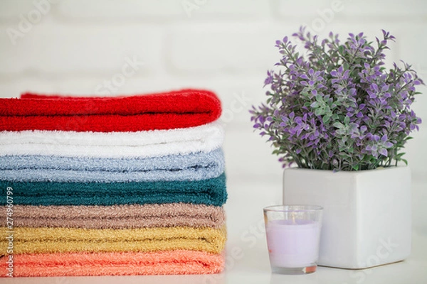 Fototapeta Fluffy bath towels on light wooden table with candle and white background