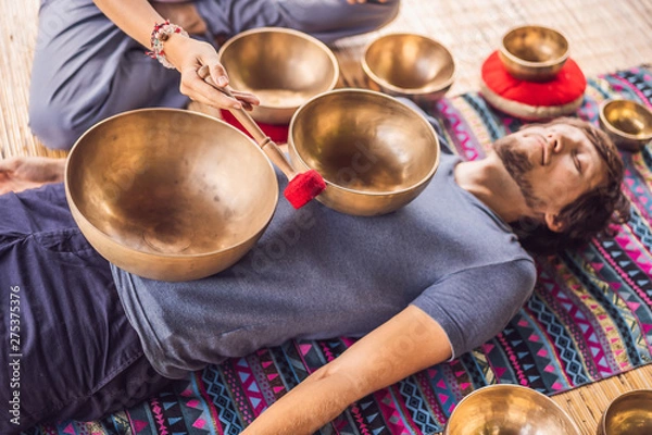 Fototapeta Nepal Buddha copper singing bowl at spa salon. Young beautiful man doing massage therapy singing bowls in the Spa against a waterfall. Sound therapy, recreation, meditation, healthy lifestyle and body