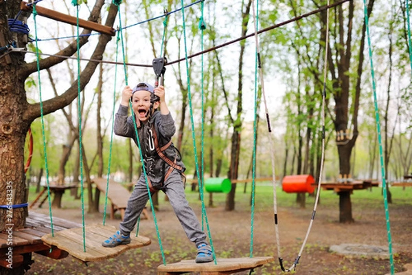 Fototapeta a little boy on an attraction in a rope Park passes an obstacle course