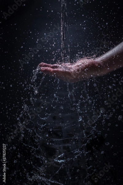 Fototapeta A Stream of Water Pouring Down a Caucasian Man's Hands - Splashing Droplets of Water Everywhere with a Black Background