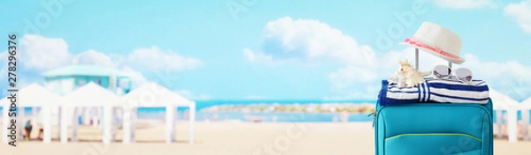 Fototapeta holidays. travel concept. blue suitcase with female hat, sea shell, sunglasses and beach towel in front of tropical background. banner