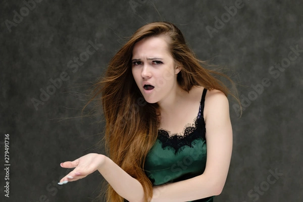 Fototapeta Concept portrait of the waist of a pretty girl, a young woman with long beautiful brown hair and a green T-shirt on a gray background. In the studio in different poses showing emotions.