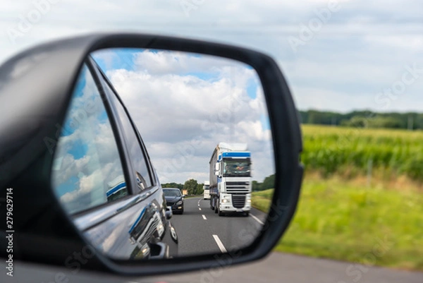 Fototapeta Asphalt road with truck reflected in car mirror.