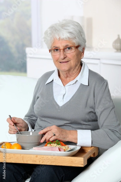 Fototapeta Elderly woman sitting in sofa  with lunch tray