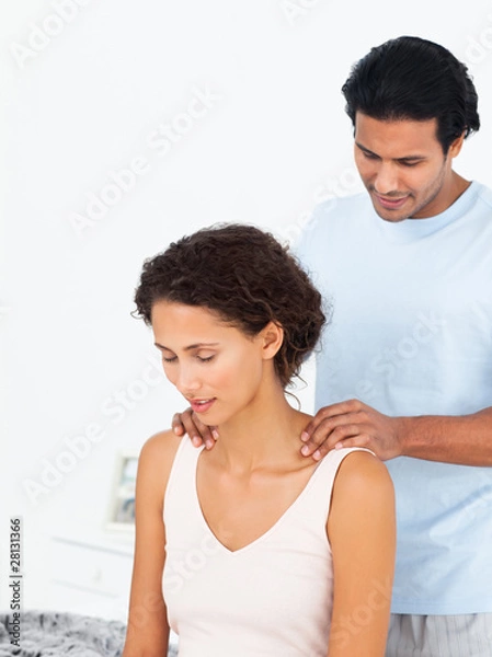 Fototapeta Hispanic man massaging his girlfriend sitting on their bed