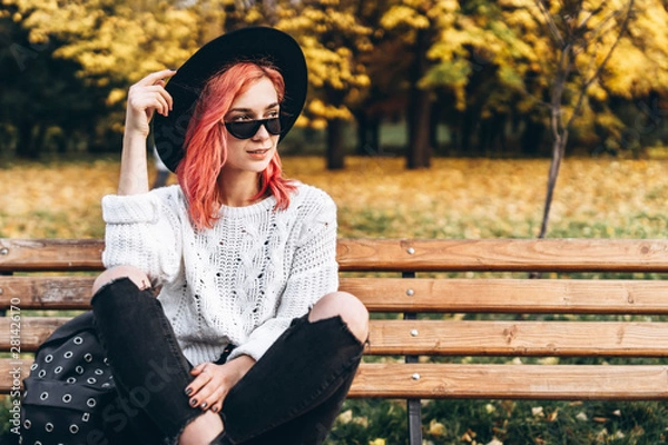 Fototapeta Pretty girl with red hair and hat relaxing on the bench in the park, autumn time.