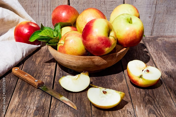 Fototapeta Fresh red apples with green leaves on a wooden old table. On a wooden background with sliced apple. Free space for text. soft focus