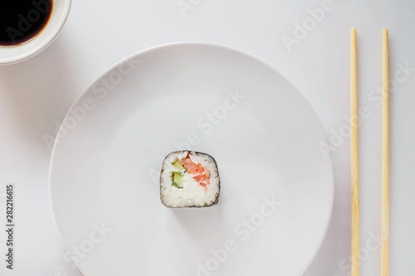 Fototapeta One Sushi Roll on white plate with chopsticks. Roll made of Fresh Raw Salmon, Cream Cheese and cucumber. Isolated on white background. Japanese seafood sushi roll on a white background.