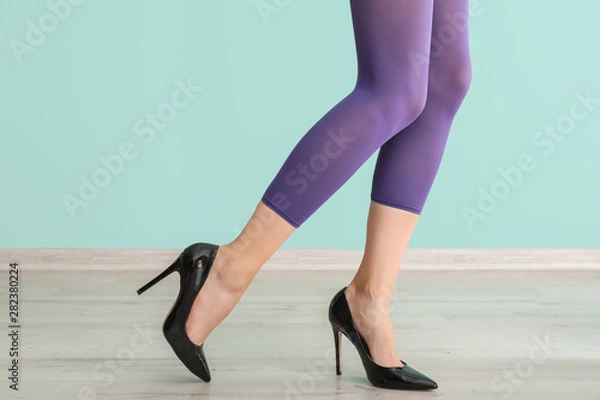 Fototapeta Stylish young woman in high-heeled shoes shoes and tights near color wall