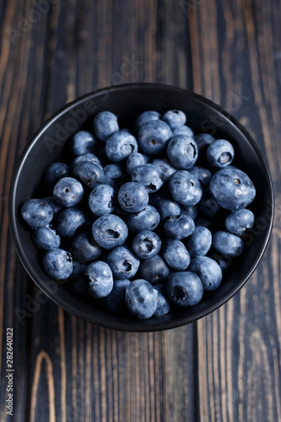 Fototapeta Handful blueberry berries in a black bowl on wooden brown table. Vitamin C and antioxidants- healthy diet food. Vertical.